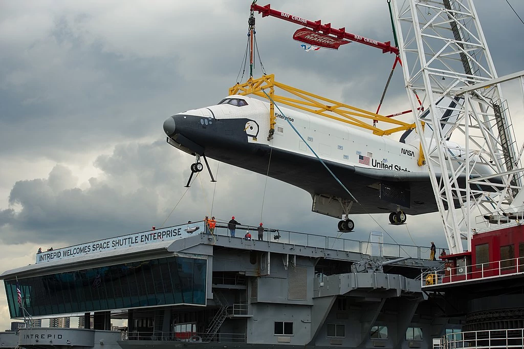 A photograph of the Spaceshuttle Entreprise being lowered on the deck of the USS Intrepid.