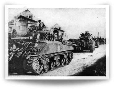 Sherman tanks advance upon a road.